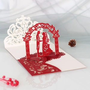 Makro-Detail der lasergeschnittenen 3D-Hochzeitskarte mit rotem Glitzer-Paar unter Blumenbogen