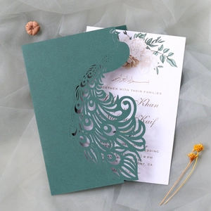 Close-up of laser-cut peacock wedding invitation with floral insert card on mesh background