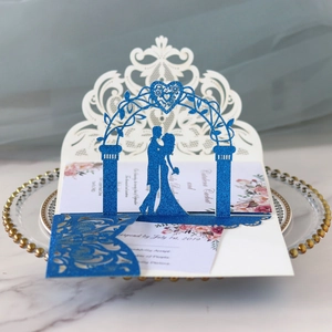 Detail of laser-cut wedding invitation featuring blue glitter silhouette on white lace base
