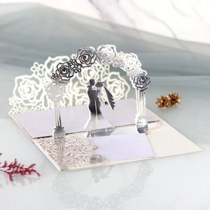 Close-up of laser-cut 3D wedding invitation featuring a bride and groom under a floral arch