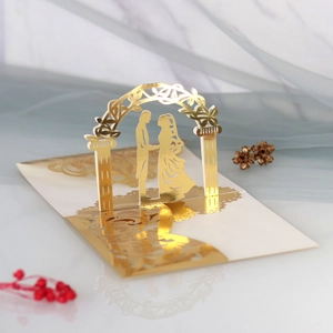 Close-up of golden 3D laser-cut wedding card featuring a romantic couple under a floral arch