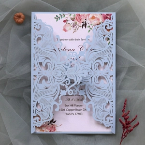 Detail of laser-cut light blue wedding invitation with floral insert and ribbon on tulle