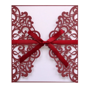 Close-up of deep red laser-cut floral invitation cover with ribbon bow and white insert