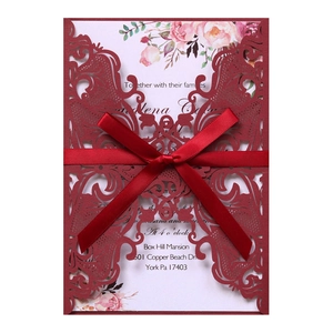Close-up of laser cut wine red wedding invitation with elegant red ribbon bow detail