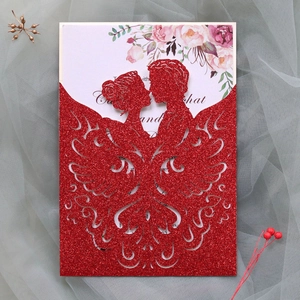 Close-up of laser-cut red glitter wedding invitation with bride and groom silhouette