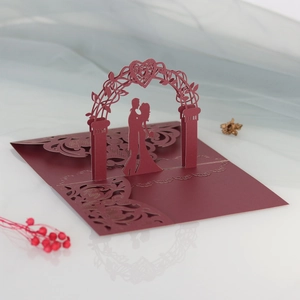 Detail of laser-cut 3D wedding invitation with couple under a heart arch in burgundy