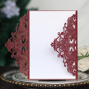 Detail of burgundy laser-cut wedding invitation with elegant vine patterns and white insert