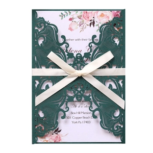 Detailed laser-cut dark green wedding invitation with white ribbon bow and floral insert