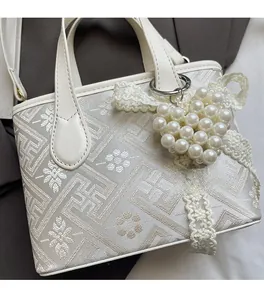 Close-up of cream textured fabric bag with pearl heart pendant and lace ribbon detail