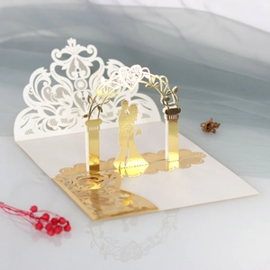 Detail of 3D laser-cut wedding card featuring a gold foil gate and kissing couple silhouette