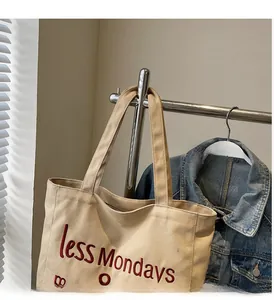 Detail of off-white canvas tote bag featuring red less Mondays embroidery and sturdy handles
