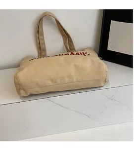 Detailed close-up of beige canvas tote bag with red more sundays letter embroidery