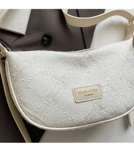 Detail of beige crescent bag showing embroidered fabric texture and leather logo patch