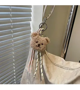 Detail eines braunen Plüschbären-Anhängers mit Webseilen an einer beige Tasche