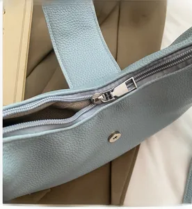 Détail du sac bleu clair à motif litchi avec fermeture éclair en métal argenté et boucle aimantée