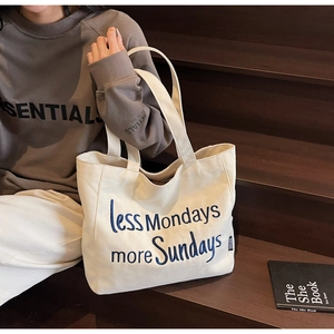 Detail of off-white canvas tote bag with blue 'less Mondays more Sundays' embroidery