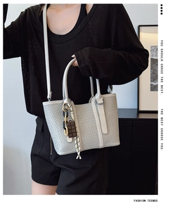 Détail du sac cabas gris clair à texture tissée avec breloque porté par un mannequin