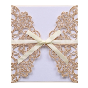 Detail view of champagne gold glitter laser-cut wedding invitation with a satin ribbon bow