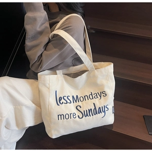 Detail of off-white canvas tote bag with blue embroidered less Mondays more Sundays text