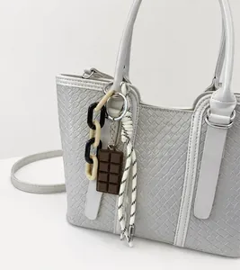 Détail d'un cabas beige en cuir tressé avec charm chocolat et bandoulière chaîne bicolore