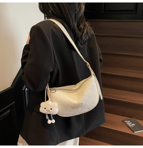 Detail of a creamy white half-moon shoulder bag with floral texture and plush cloud charm