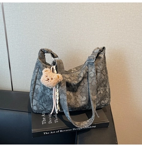 Detail der grauen Jacquard-Tasche mit Blumenmuster, Plüschbär-Anhänger und breitem Gurt