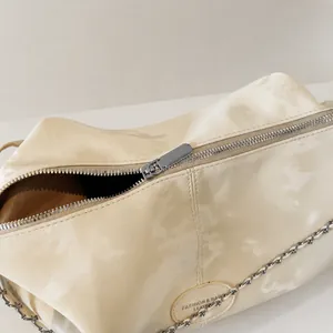 Detail of silver smooth zipper and chain strap on cream white glossy PU tote bag
