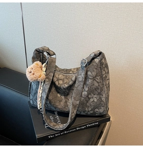 Detail der grauen Tragetasche mit Blumenmuster und Teddybär-Anhänger auf Büchern