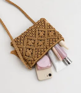 Detailed view of khaki woven crossbody bag with tassels and cosmetic items on white cloth