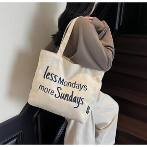 Detail of cream canvas tote bag featuring navy blue Less Mondays more Sundays embroidery
