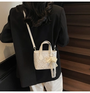 Close-up of a white mini bucket bag with floral texture and pearl lace bow detail