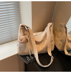 Detail der beigen Halbmond-Schultertasche mit braunem Plüschbären-Anhänger und Webriemen