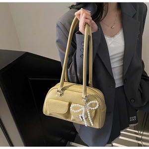 Detail of yellow lychee leather shoulder bag featuring a pearl bow charm and side pockets