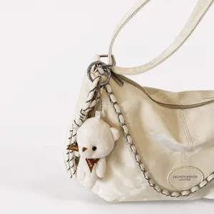 Detail of cream shoulder bag with silver chain strap and cute teddy bear charm accessory