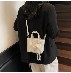 Crossbody view of a cream mini bucket bag with geometric patterns and pearl charm