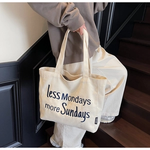 Detail of canvas tote bag featuring embroidered blue lettering less Mondays more Sundays