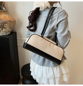Minimalist beige woven pillow bag with black leather trim worn on shoulder with white skirt