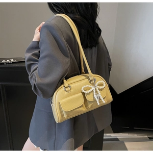 Detail of yellow pebbled leather shoulder bag with front flap pockets and pearl bow charm