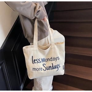 Detail of canvas tote bag with embroidered blue 'less Mondays more Sundays' text