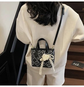 Detail of crossbody bucket bag with geometric maze pattern and pearl lace bow accessory
