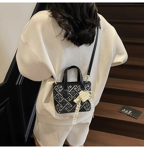 Detail of crossbody bag with geometric pattern and pearl bow charm on a leather surface