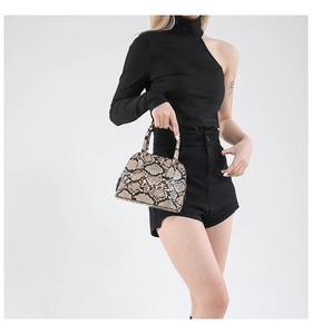 Close-up of snake skin print shell bag carried by a model in black elegant outfit