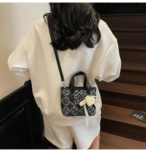 Detail of crossbody bucket bag featuring black and white geometric patterns and pearl charm