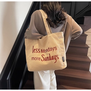 Detail of canvas tote bag featuring red embroidered slogan less Mondays more Sundays