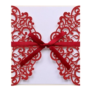 Detail of red laser cut wedding invitation with intricate lace pattern and satin ribbon