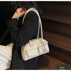Detail of a beige leather pillow bag showing front flap pockets and a pearl bow charm