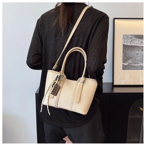 Détail d'un sac cabas tissé beige avec pendentif chocolat et bandoulière réglable