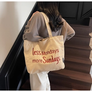Detail of beige canvas tote bag featuring red embroidered text on a wooden staircase