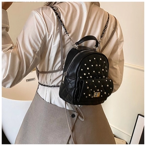 Quilted black mini backpack with silver rivets shown on model in a modern interior