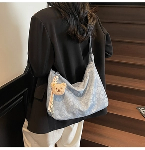 Detail einer floralen Denim-Tasche mit Bärenanhänger an einem Modell im Innenraum